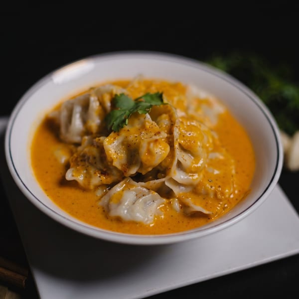 A white bowl filled with dumplings in a rich orange sauce, garnished with fresh cilantro.