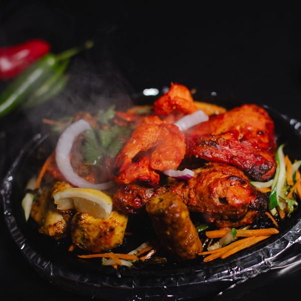 Steaming hot Indian sizzler platter with chicken tikka, prawns, seekh kebab, and vegetables.
