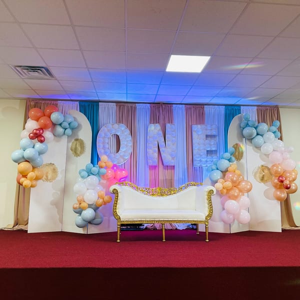 A stage with a white and gold sofa, balloon arches, and "ONE" spelled out in large letters.