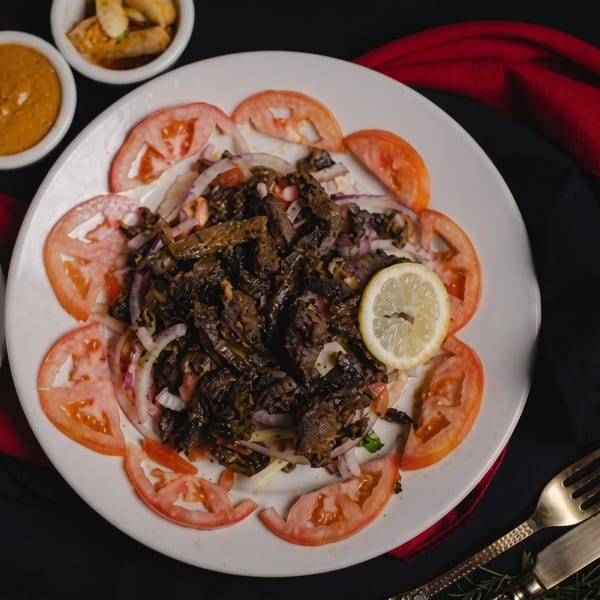 A white plate of dark meat and onions, garnished with tomato slices and a lemon wedge.