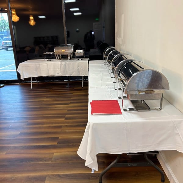 Two buffet tables with white tablecloths and several chafing dishes in a restaurant setting.