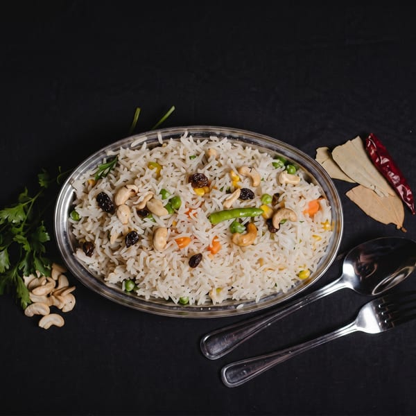 A silver platter of white rice with cashews, raisins, peas, and carrots on a black tablecloth.