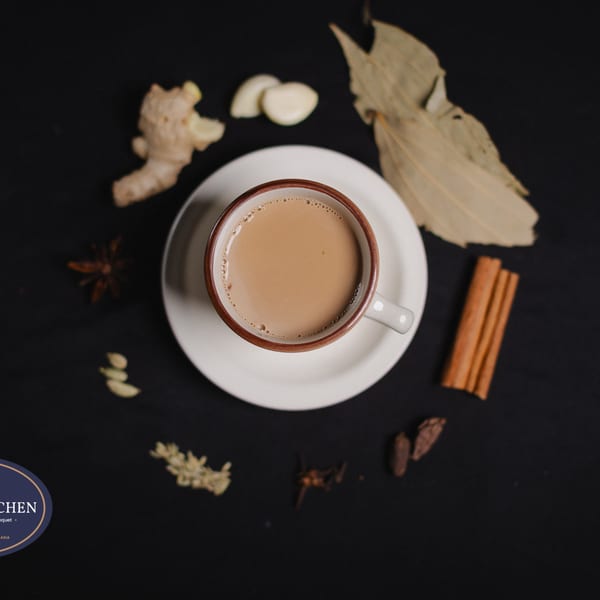 Overhead view of a cup of chai tea surrounded by spices like ginger, garlic, and cinnamon sticks.