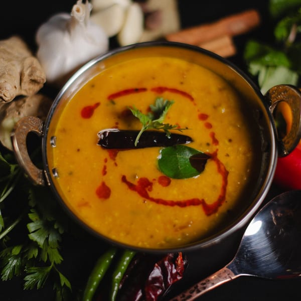 A bowl of yellow lentil dal with red chili oil, a dried chili, and cilantro garnish.