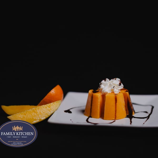 A mango pudding dessert with whipped cream and chocolate drizzle, served with mango slices.