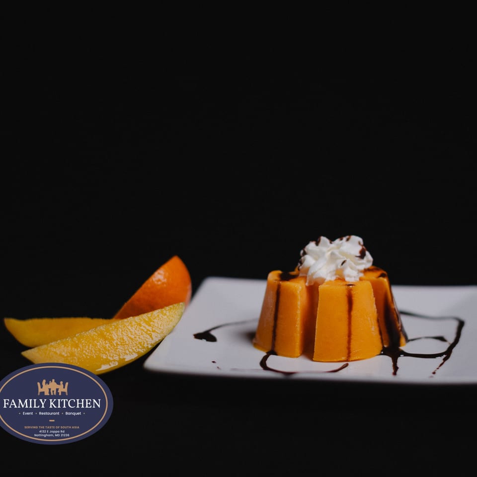 A mango pudding dessert with whipped cream and chocolate drizzle, served with mango slices.