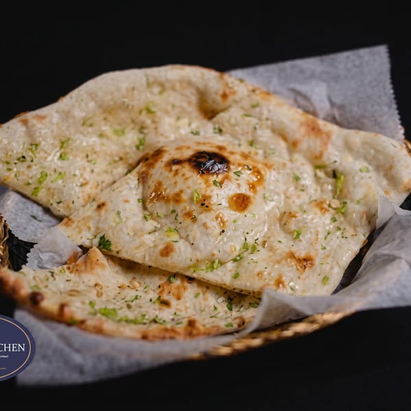 Golden-brown naan bread, garnished with green herbs, served in a basket lined with white paper.
