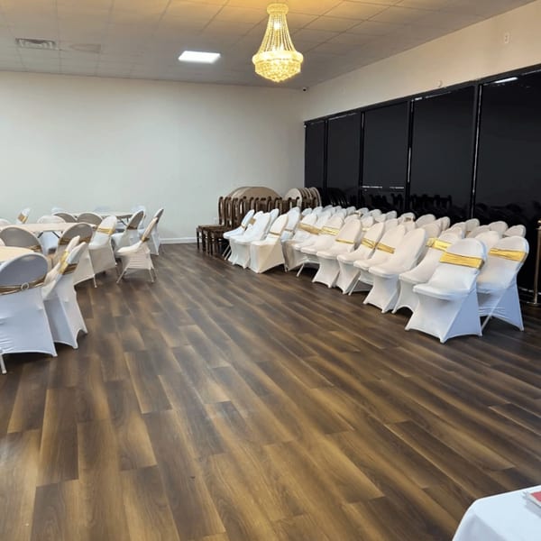 Empty event hall with rows of white chairs with gold sashes and round tables with white tablecloths.