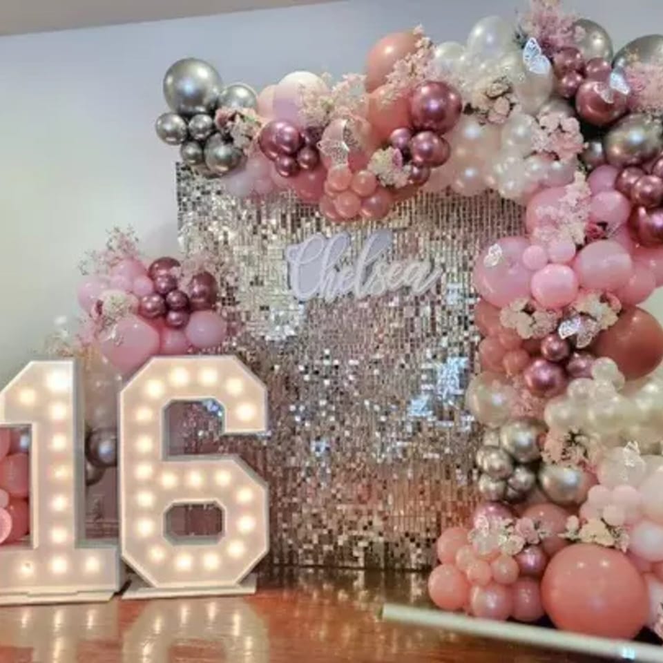 A pink and silver balloon arch with a sequin backdrop, light-up "16" numbers, and "Chelsea" sign.