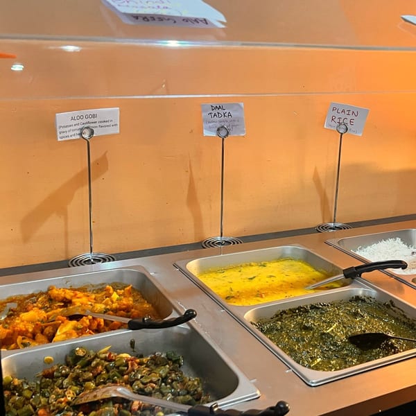 A buffet line with trays of Indian food, including Aloo Gobi, Daal Tadka, and Plain Rice.
